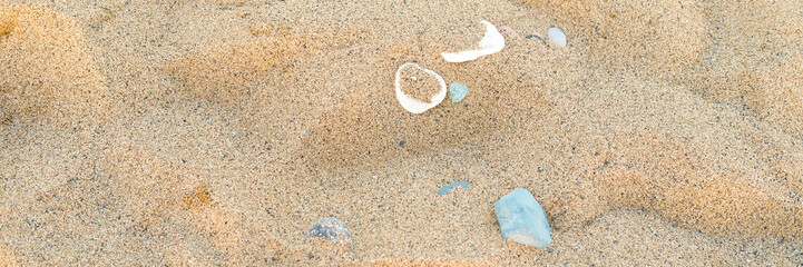 Close-up view of various seashells and colorful stones scattered on golden sandy beach, showcasing...