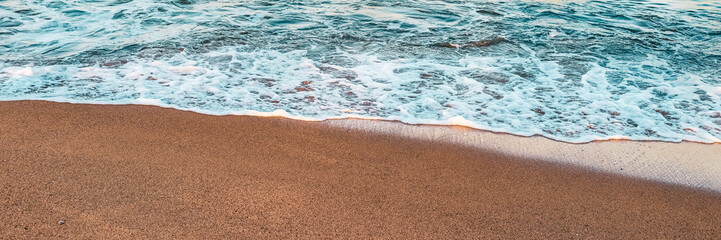 Calm sea waves lapping the sandy beach at sunset create a tranquil coastal atmosphere with soft colours and textures, perfect for relaxation and beach holidays. Banner with copy space