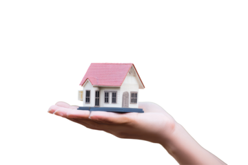 A miniature house with a pink roof held in a hand against a stark black background creating contrast and focus on transparent background