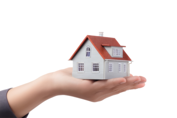 Hand holding a miniature white house with a red roof against a black background in a studio shot on transparent background