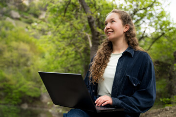 Portrait of dreamy young woman with curly hair looking up during using laptop pc computer sitting...