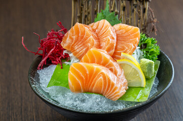 A plate of delicious fresh salmon sashimi served on ice with lemon and greens.