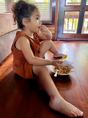 Cute Asian little girl with blond hair eating stir-fried rice noodles with soy sauce