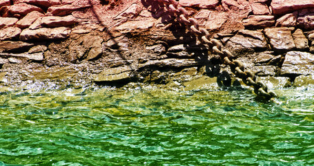 Rusty chain hanging over greenish water surface