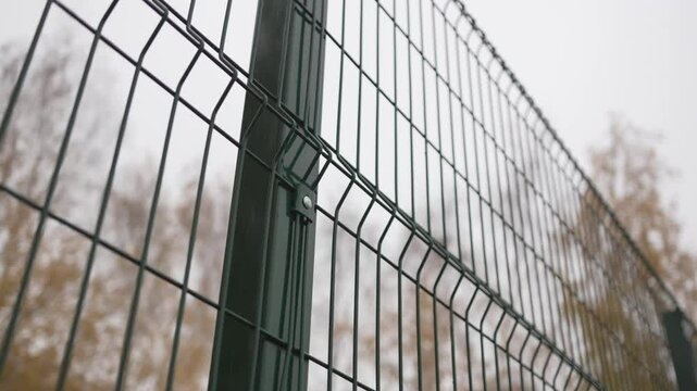 Wired fence shows structured pattern near football field closeup. Sharp metal lines frame view of empty sports zone during cold season