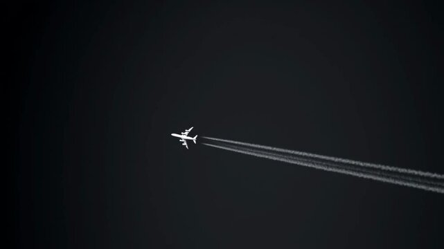 Passenger jet soaring through stormy sky, trailing vibrant white condensation stream against black background. Jet airplane flying high against dark sky,