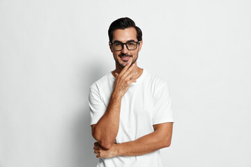 Fototapeta premium Handsome man in casual white t-shirt and glasses smiling confidently while looking at the camera with thoughtful expression isolated on plain light background.