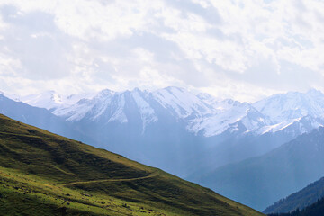 Fototapeta premium a mountain road on a slope with a view of the snowy peaks. Morning in the mountains