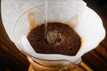 Close-up of hot water being poured over coffee grounds in a paper filter during manual pour-over brewing using a glass