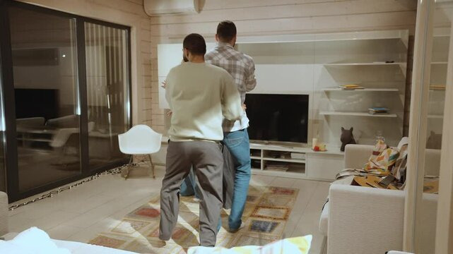 Two adult men and two women dance in a conga line across a cozy modern living room. They wear casual clothes and smile, moving together in a playful atmosphere during the evening at home.