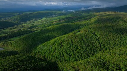 Rolling green hills and mountains under blue sky with clouds in early morning sunlight in West...