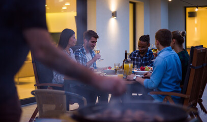 A group of young diverse people having dinner on the terrace of a modern house in the evening. Fun for friends and family. Celebration of holidays, weddings with barbecue