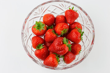 Fresh strawberries in cut glass bowl against a white background.