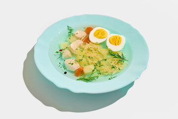 Clear soup with diced chicken, potato cubes, sliced carrots, half boiled egg and noodles served in pastel blue plate garnished with fresh dill and peppercorns. Concept of food, nutrition
