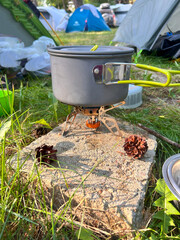 Camping pot on a gas stove among grass and tents