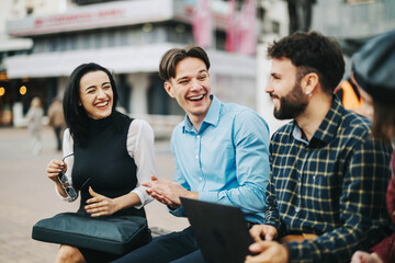 A group of diverse young professionals are laughing and talking outside. They appear relaxed and...