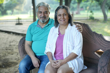 Indian happy senior couple sitting at bench at park. Happy Old man and woman relaxing at park spend time together, relationship and people concept. Senior Living Retirement and Pension Plans Concept 