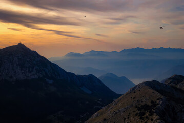 Scenic sunset over a dramatic mountain range with layered ridges fading into the distanc