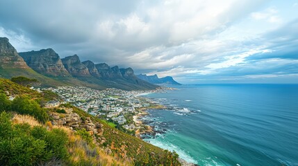 stunning view of the coastal city of Cape Town, with the dramatic backdrop of mountain slopes, urban buildings, and the sparkling ocean under a cloudy sky.