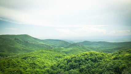 Obraz premium Vast green hills and a hidden lake under a clear sky in the Georgian countryside. Peaceful and expansive natural landscape from a high vantage point