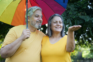 Monsoon Bonanza Senior couple Concept. Indian senior couple under rainbow umbrella at park. Asian...