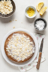 Homemade rustic cake, decorated with almonds and white sugar on wooden table.  Some ingredients are: eggs; sugar; flour; butter., lemond Top View.
