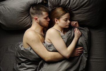 Young couple resting closely in bed, deeply asleep while embracing each other. Intimacy captured in...