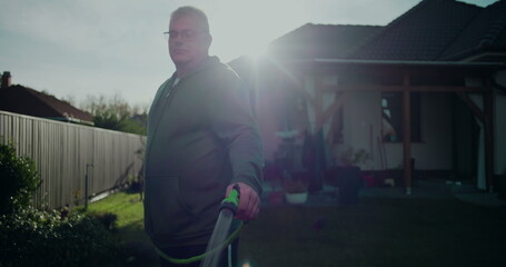 Man holding garden hose in backyard, standing near residential house, casual moment in suburban...