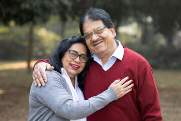 Fototapeta premium Indian happy elderly couple embracing in outdoor park. Asian Happy loving Senior Couple having fun in vacation time. Senior citizens care hugging or date at the park for romance after retirement