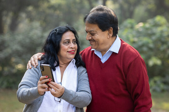 Indian senior happy couple using mobile phone at the park. Mobile Banking everywhere