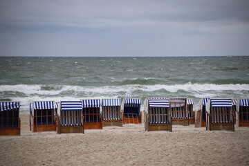 Empty  hooded beach chairs (strandkorbs) lined up on the shore under stormy spring skies, Kołobrzeg, Poland