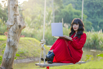 Concentrated asian woman sitting on the swing, working on laptop browsing internet at home during lazy weekend, focused young woman busy using computer surfing wireless web shopping online. 