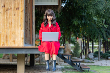 Asian woman using a laptop communicates over the Internet with a client from terrace at home. 