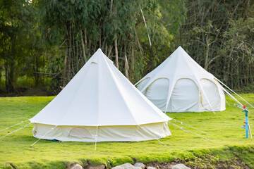 Luxury Tent at a Campsite. Two big white camping tent with camping gears in a green grass with mountains. 