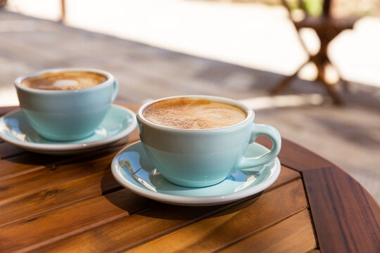 Caf&eacute; cappuccino mousseux en terrasse sur une table en bois au soleil servi dans des tasses bleues