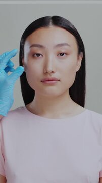Portrait of chinese female face isolatedon grey background. Cosmetologist hands injecting hyaluronic acid cheeck injection for face anti-aging skincare procedure.