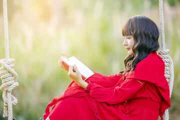 Side view young calm happy woman wear a red dress, she reading book study rest relax spend time in nature.