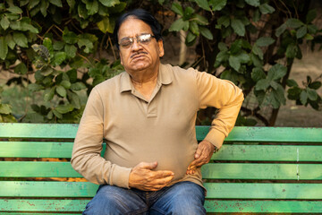 Fototapeta premium Indian painful senior man suddenly suffering stomach pain at park