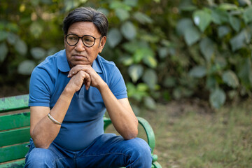 Depression, thinking, Upset lonely homeless senior man in garden sitting on bench with depression holds head in hands. Sad, worried indian mature male with thoughtful face expression