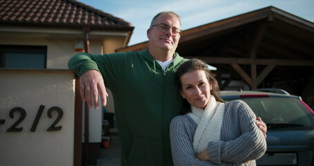 Man and woman standing together outside their home, relaxed and confident, embracing a sense of partnership, community, and connection in a residential neighborhood