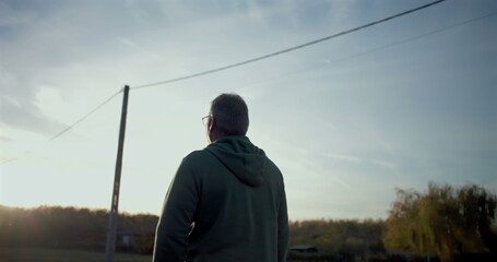 Man walking forward on a rural road, gazing ahead thoughtfully, serene open surroundings, utility...