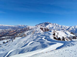 Expansive view of a snow-blanketed mountain range under a bright blue sky. The landscape features...