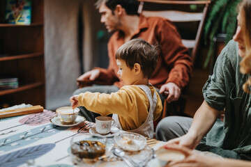 A child prepares tea at a table surrounded by family members, highlighting togetherness and warmth...