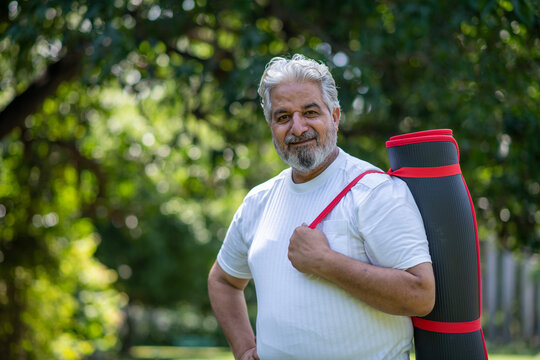 Portrait of Indian or Asian healthy happy senior man standing and looking at camera after completed yoga classes while standing at park