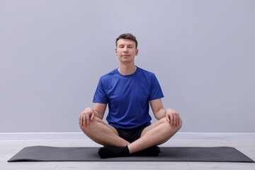 Fototapeta premium Young man practicing yoga on mat indoors