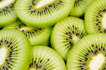 Pile of sliced kiwi fruit, with vibrant green color of fruit standing out against white background.