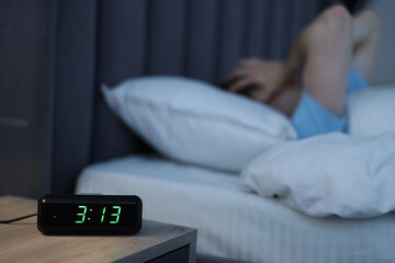Man suffering from insomnia on bed indoors, focus on digital alarm clock