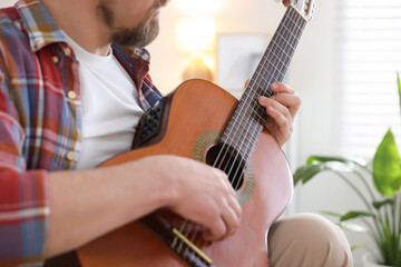 Man playing acoustic guitar at home, closeup