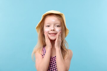 Smiling little girl with sun protection cream on her face against light blue background