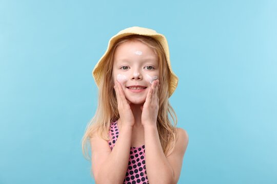 Fototapeta Smiling little girl with sun protection cream on her face against light blue background